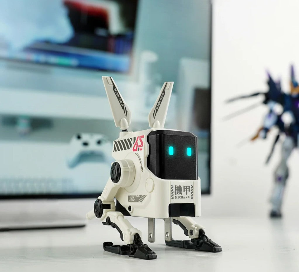 Small robot toy with a blurred background of a computer monitor and another robot model.